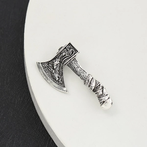 Silver vintage axe brooch with intricate carvings and textured handle on a white plate
