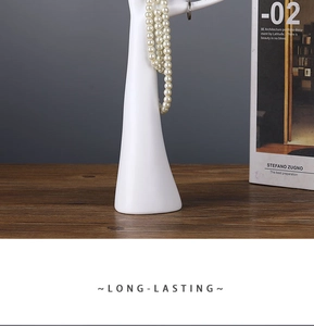 Detailed view of a white hand-shaped resin jewelry holder displaying pearl necklaces on wood