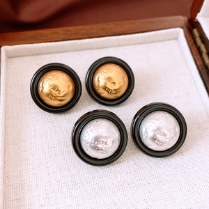 Detail shot of vintage gold and silver dome earrings with textured relief and black trim