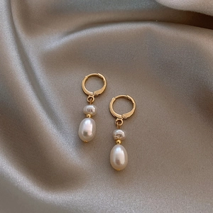 Macro detail of baroque freshwater pearl drop earrings on champagne silk fabric