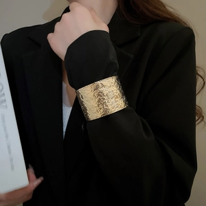 Detailed view of golden hammered texture cuff bracelet worn over a black blazer sleeve