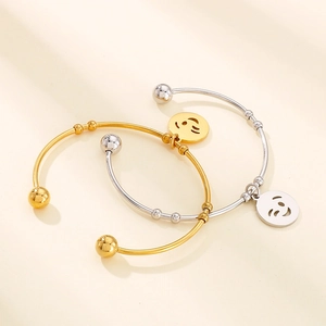Close-up of gold and silver smiley face charms on stainless steel open cuff bracelets