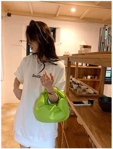 Detail of neon green ruched cloud bag showing the knotted handle and pleated leather texture
