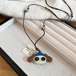 Close-up of cartoon dog pendant with blue hat in a beige jewelry box on white fabric