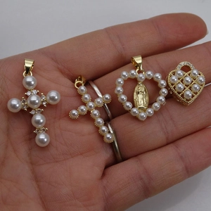 Gold plated cross and heart pendants with white pearls and zircon inlay shown in hand
