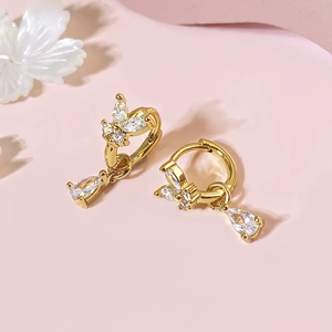 Golden butterfly earrings with sparkling cubic zirconia teardrops on a pink background
