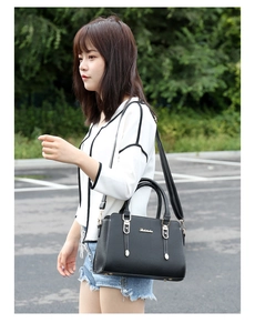 Outdoor shot of a black pebbled leather tote bag with gold hardware and shoulder strap