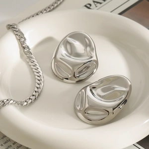 Minimalistische unregelmäßige silberne Ohrringe auf weißem Tablett mit Metallkette
