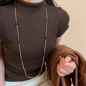Detailed close-up of tiger eye beaded necklace on a brown knit sweater surface