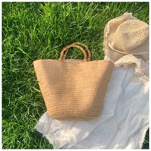 Close-up of handmade straw tote bag with bamboo handles on green grass for summer picnic
