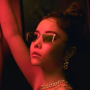 Detail of square metal sunglasses and bold chain necklace on model in red light
