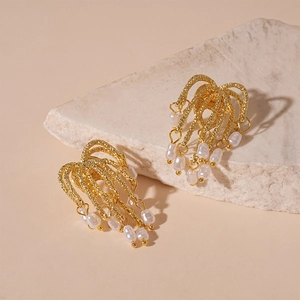 Detail of gold metal firework fringe earrings with white imitation pearl drops on stone