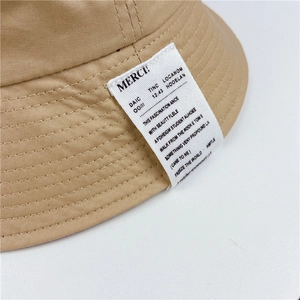 Close-up of khaki bucket hat showing woven patch with MERCI text and cotton twill texture