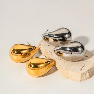 Polished gold and silver teardrop earrings displayed on a natural travertine stone base