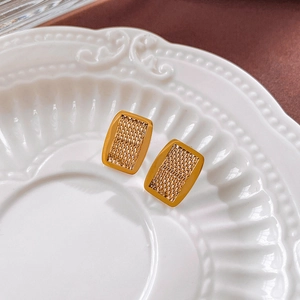 Close-up of golden rectangular mesh earrings with woven texture on a ceramic plate