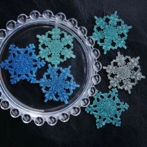 Set of 6 glittery resin snowflakes in blue and white on a black textured background