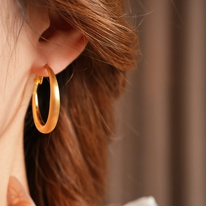 Close-up of matte golden geometric round hoop earrings worn by a female model