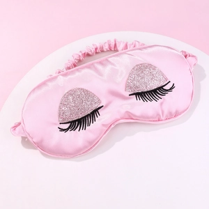 Pink satin sleep mask with sequin eyelash detail on a white circular stand