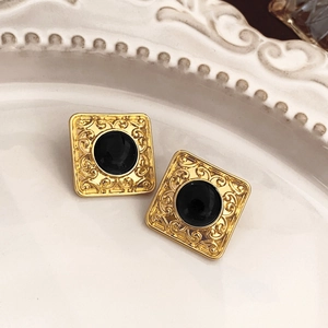 Detail of vintage gold square earrings with round black stones on a white ceramic plate