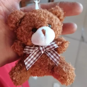 Close-up of a dark brown plush bear keychain featuring a checkered bowtie and soft texture