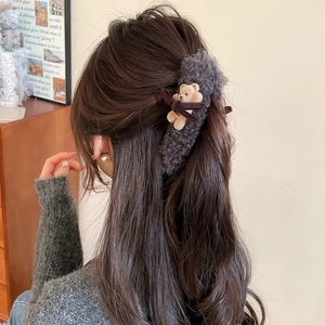 Close-up of a grey plush hair clip featuring a cute brown 3D bear and a dark bow detail