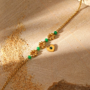 Detailed view of golden chain bracelet with green beads and heart-shaped gemstone charm