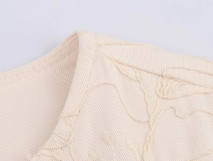 Macro shot of off-white twill jacket fabric featuring detailed embroidery and seam edging