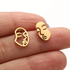 Golden abstract face stud earrings with asymmetric hollow design shown on finger