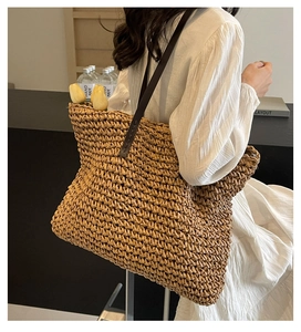 Close-up of woven straw tote bag with brown leather straps shown on model in minimal setting