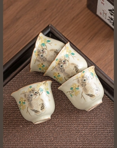 Detailed view of four ceramic Ru-kiln tea cups with hand-painted cats in a woven tray