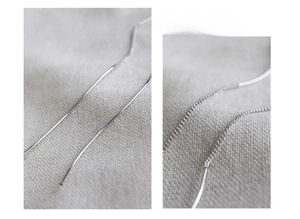 Macro detail of S925 sterling silver long threader earrings on textured beige linen