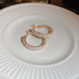 Macro detail of gold hoop earrings with square zircon crystals on a white ceramic plate