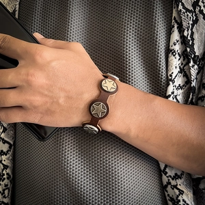 Close-up of a vintage dark brown leather bracelet with silver star rivets on a wrist
