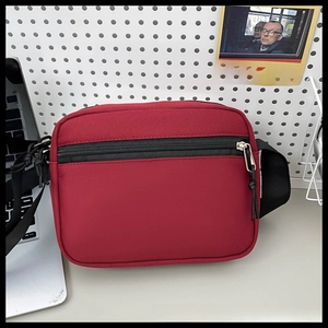Close-up of a durable wine red nylon crossbody bag with black zipper on a desk