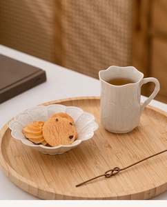 Detail of creamy white ceramic cup and petal-shaped bowl with plant relief texture on wood tray
