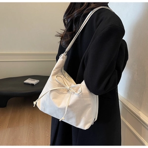 Detail of white canvas shoulder bag featuring a drawstring bow and minimalist texture