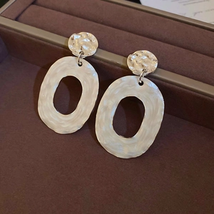 Detailed view of silver-tone hammered texture and white drop oil oval drop earrings