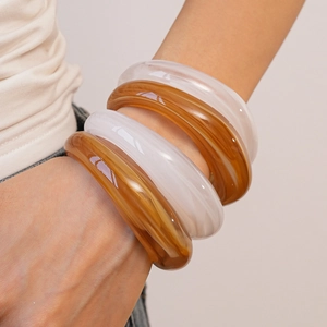 Close-up of four chunky acrylic bangles in marble amber and milky white on wrist