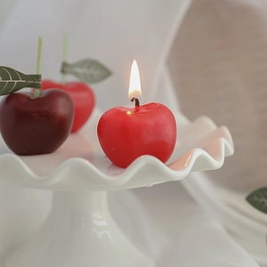 Velas aromáticas con forma de cereza roja y granate sobre un plato de cerámica blanca