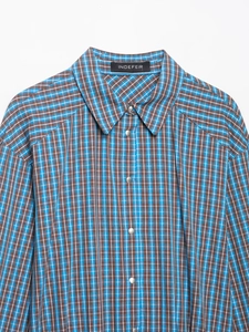 Détail de chemise à carreaux bleu et marron avec col pointu et boutons pression argentés