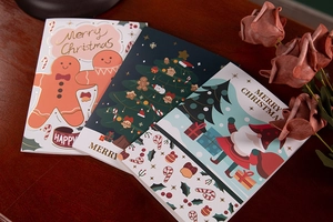 Three festive Christmas cards with gold foil designs on a warm wooden table background