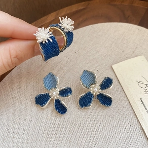 Detail of denim fabric C-shaped earrings with white floral petals and pearl center