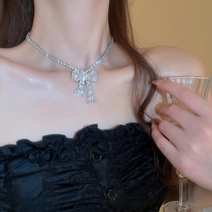 Detail of silver bow pendant necklace featuring sparkling crystals worn by model