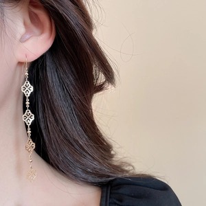 Detail of elegant gold drop earrings with delicate four-leaf clover cutouts and bead chains