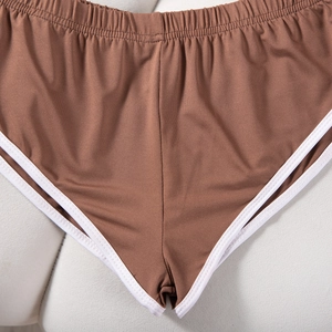 Detail der braunen Yogahose mit weißer Kontrastpaspel und elastischem Bund auf beigem Grund