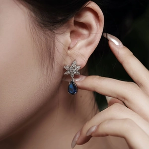 Macro shot of a teardrop blue gemstone earring with floral zircon accents on a model