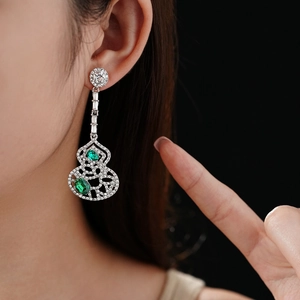 Close-up of hollow gourd pendant earrings with green gemstones and sparkling zircons