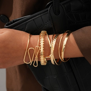 Détail de 6 bracelets géométriques dorés superposés avec une texture métallique
