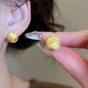 Close-up of golden brushed sphere stud earrings showing detail and wearing effect