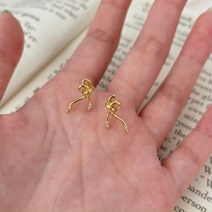 Detailed view of gold bow earrings with micro-inlaid zircons held in a hand